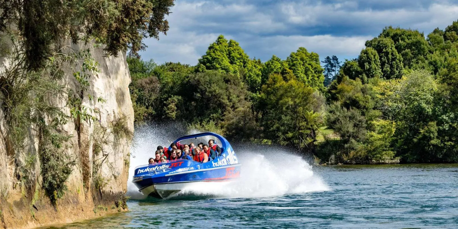 Hukafalls Jet boat turning beside a tree-lined river cliff